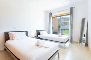 A hotel room with two beds, a large window with curtains, and a view of a building outside.