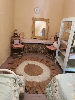 Ein gemütliches Zimmer mit einem Kamin aus Stein, zwei Holzstühlen, einem runden Teppich und einer Spiegelwand.