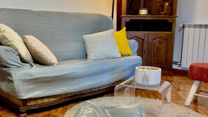 Una sala de estar con un sofá gris, un aparador de madera y una mesita de vidrio con una vela blanca.