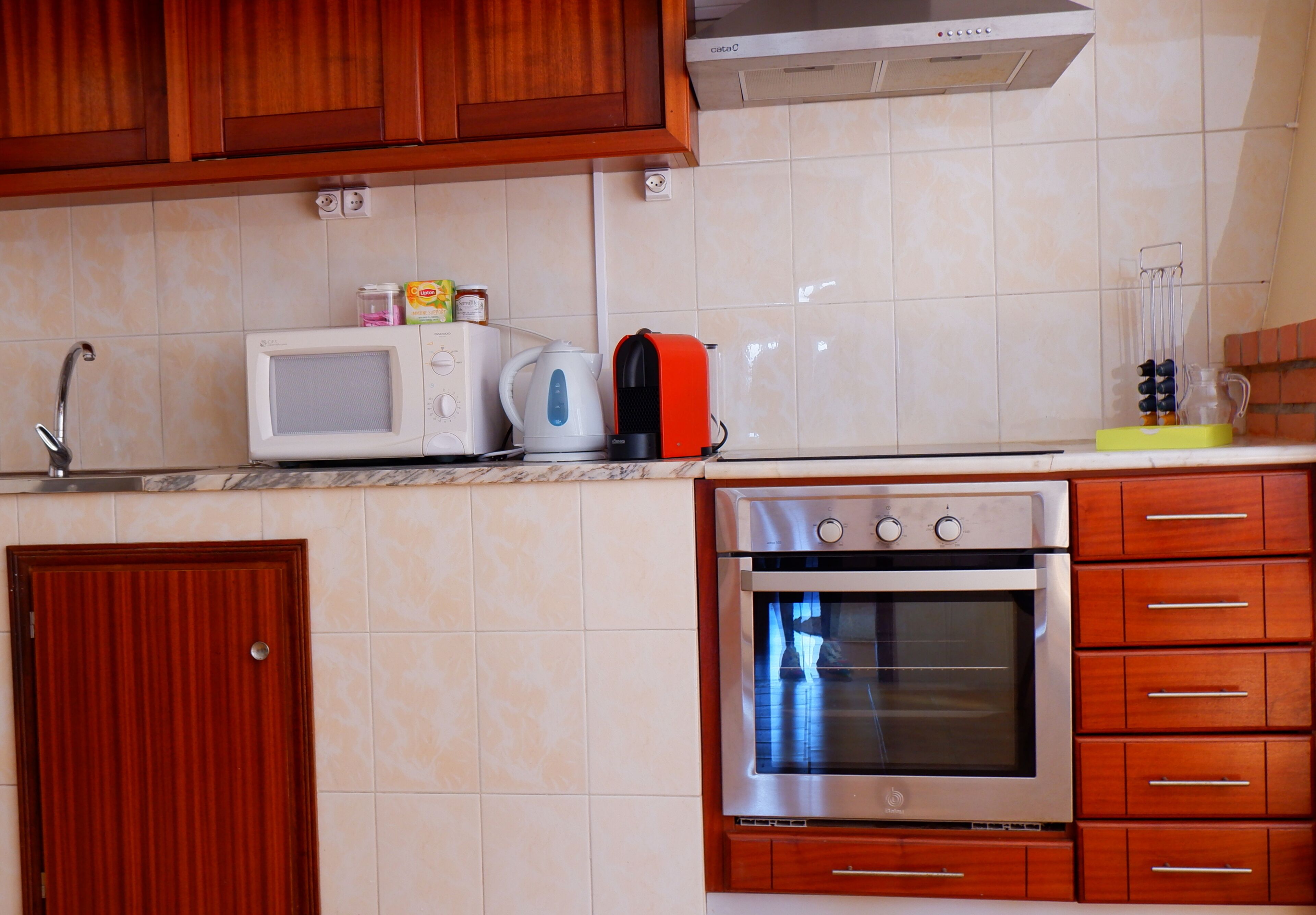 Una cocina con armarios de madera, microondas, hervidor y horno empotrado.