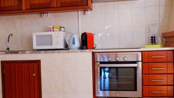 Una cocina con armarios de madera, microondas, hervidor y horno empotrado.