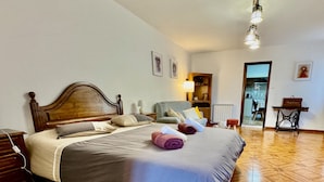 Una cama bien tendida con cabecera de madera, una mesita de noche con lámpara y una silla en una habitación con suelo de espiga.