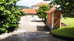 A courtyard with a stone wall, a small building with a tiled roof, and a grassy area. - Casa Outeiro 99 Paredes de Coura (Paredes de Coura)