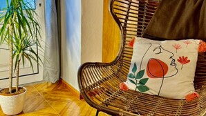 Una silla de mimbre con un cojín floral, una planta en maceta y una puerta de madera al fondo.