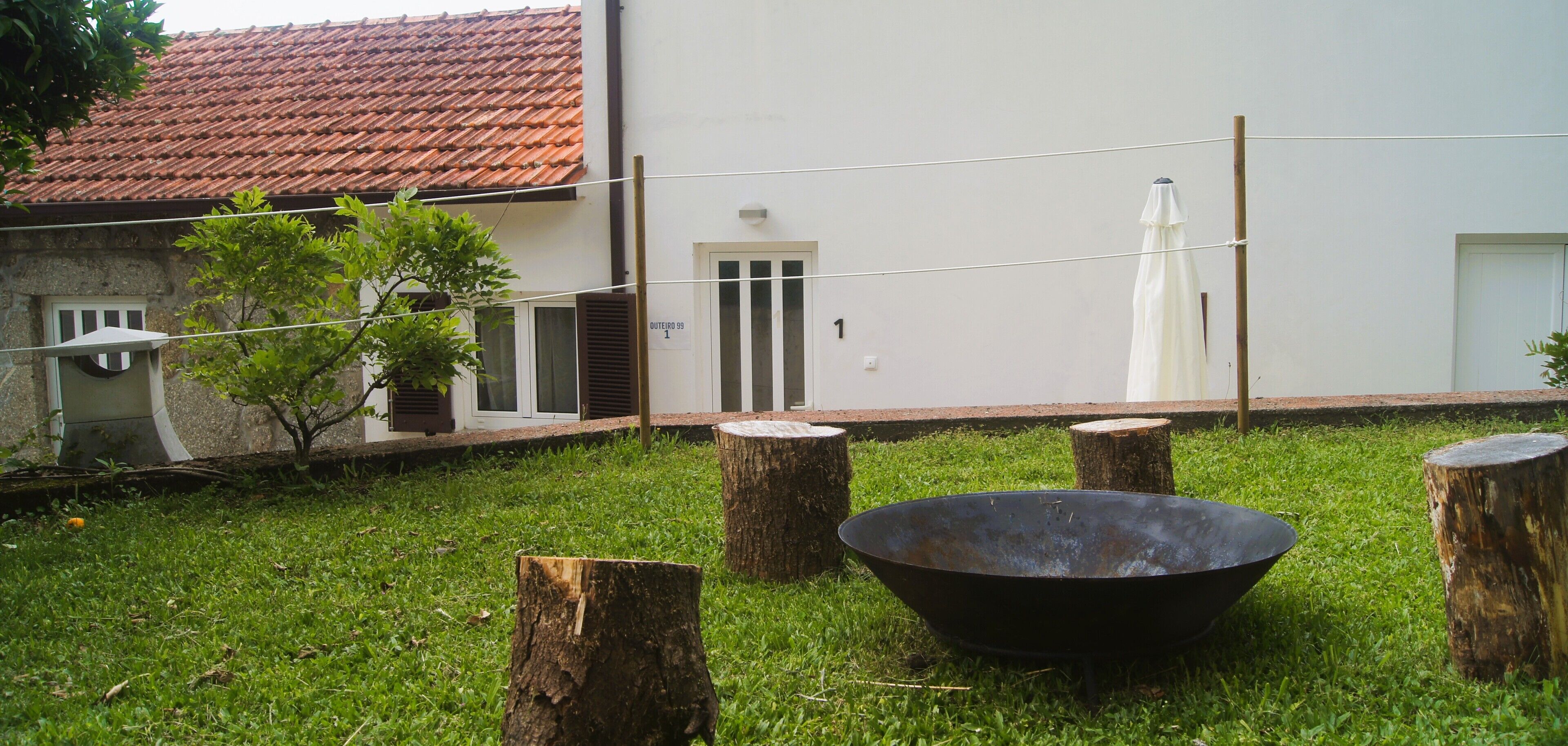 A grassy yard with a metal bowl, wooden stumps, and a building with a tiled roof and a door marked "1".