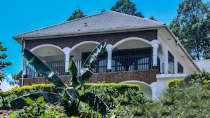 A two-story house with a balcony, surrounded by lush greenery and trees. - The Fortuna Hotel and Cafe (Kabale)