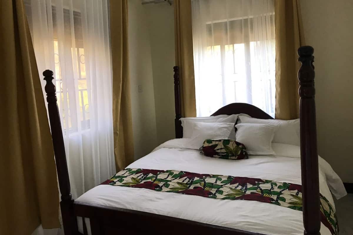 A four-poster bed with white linens and a floral bedspread, in a room with beige curtains and a wooden headboard.