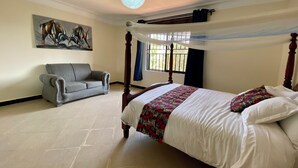 A bedroom with a four-poster bed, a grey sofa, a large painting on the wall, and a ceiling light fixture. - The Fortuna Hotel and Cafe (Kabale)
