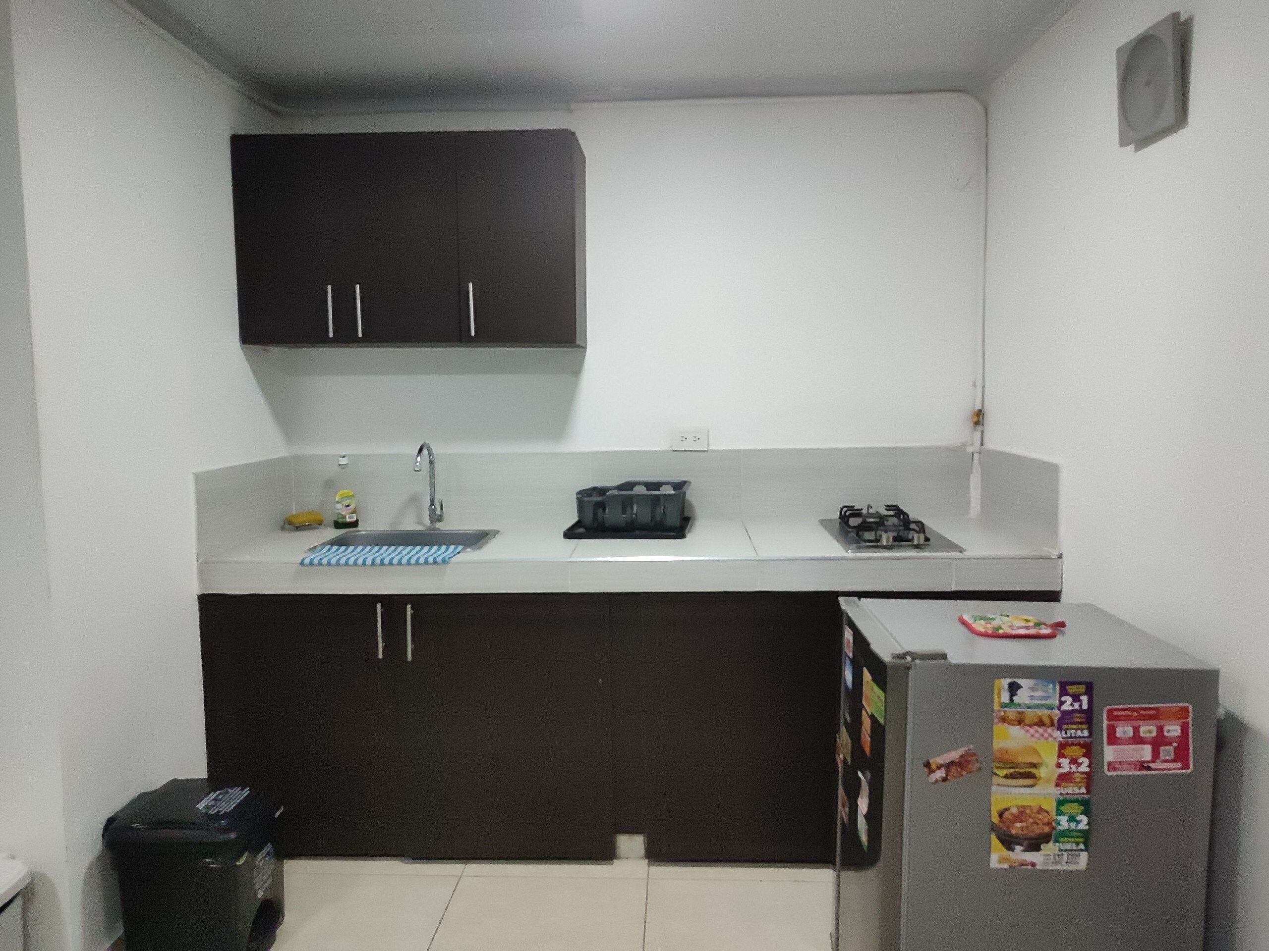 A compact kitchen with dark cabinets, a sink, a stove, and a refrigerator.