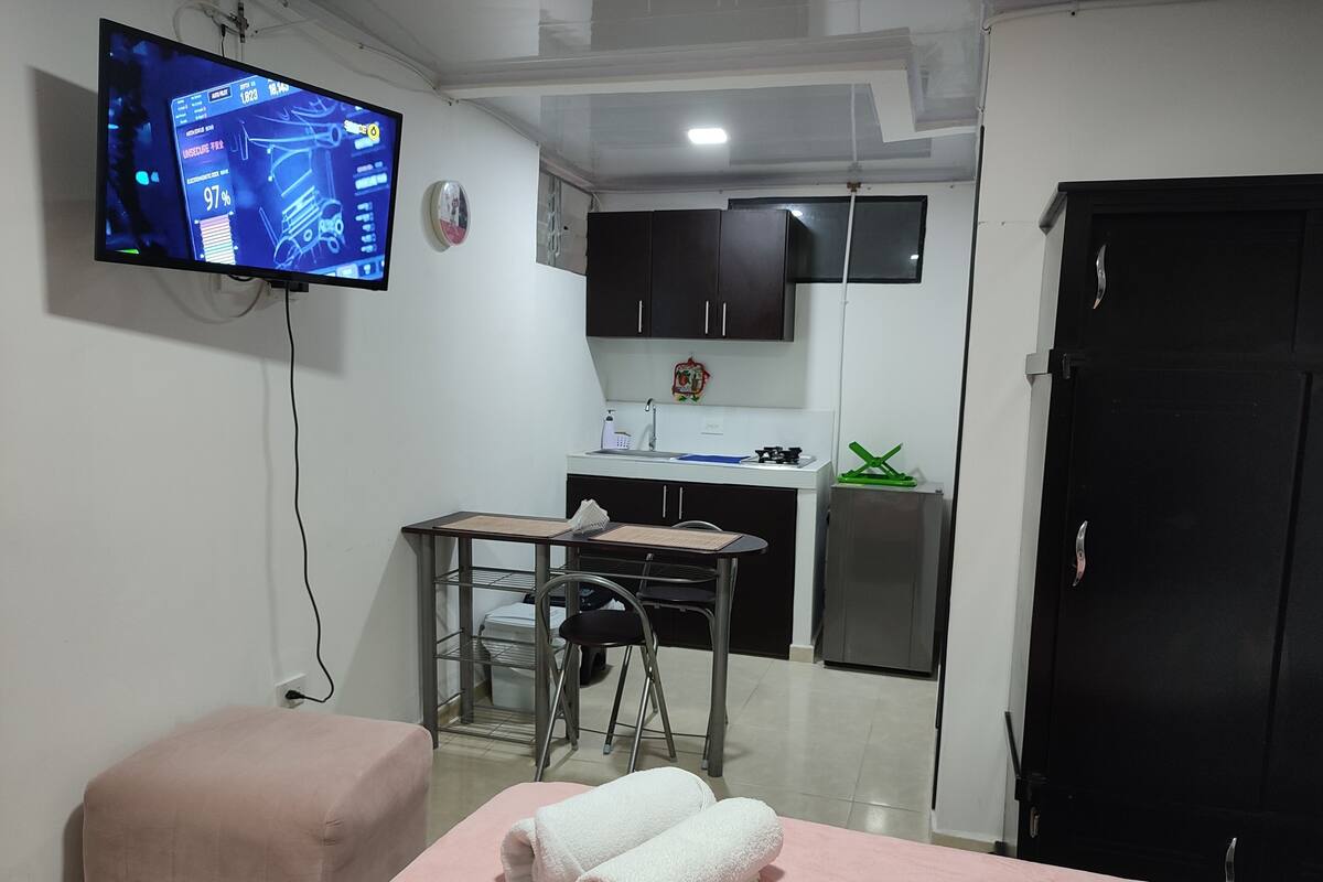 A small room with a bed, a table, a chair, a TV, a sink, and a cabinet.