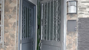 A set of double doors with decorative metalwork, a stone wall, and a security camera mounted above the door. - Casa Confort (Pereira)