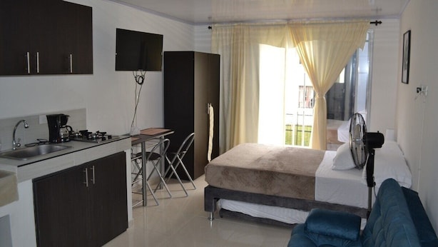 A compact hotel room with a kitchenette, a bed, a small table, and a chair. - Casa Confort (Pereira)
