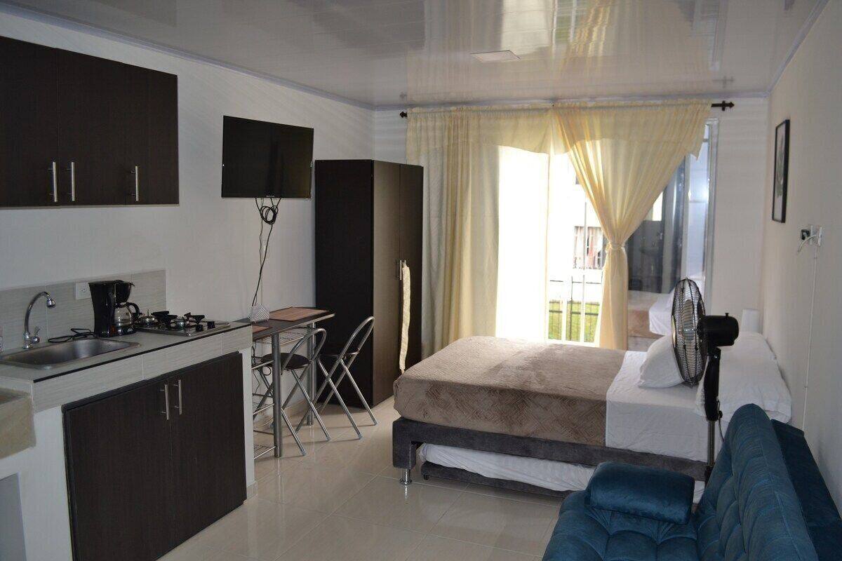 A compact hotel room with a kitchenette, a bed, a small table, and a chair.