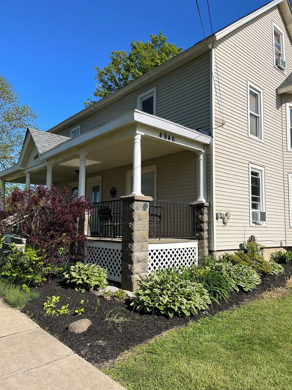 A two-story house with a covered porch, stone pillars, and a mailbox.