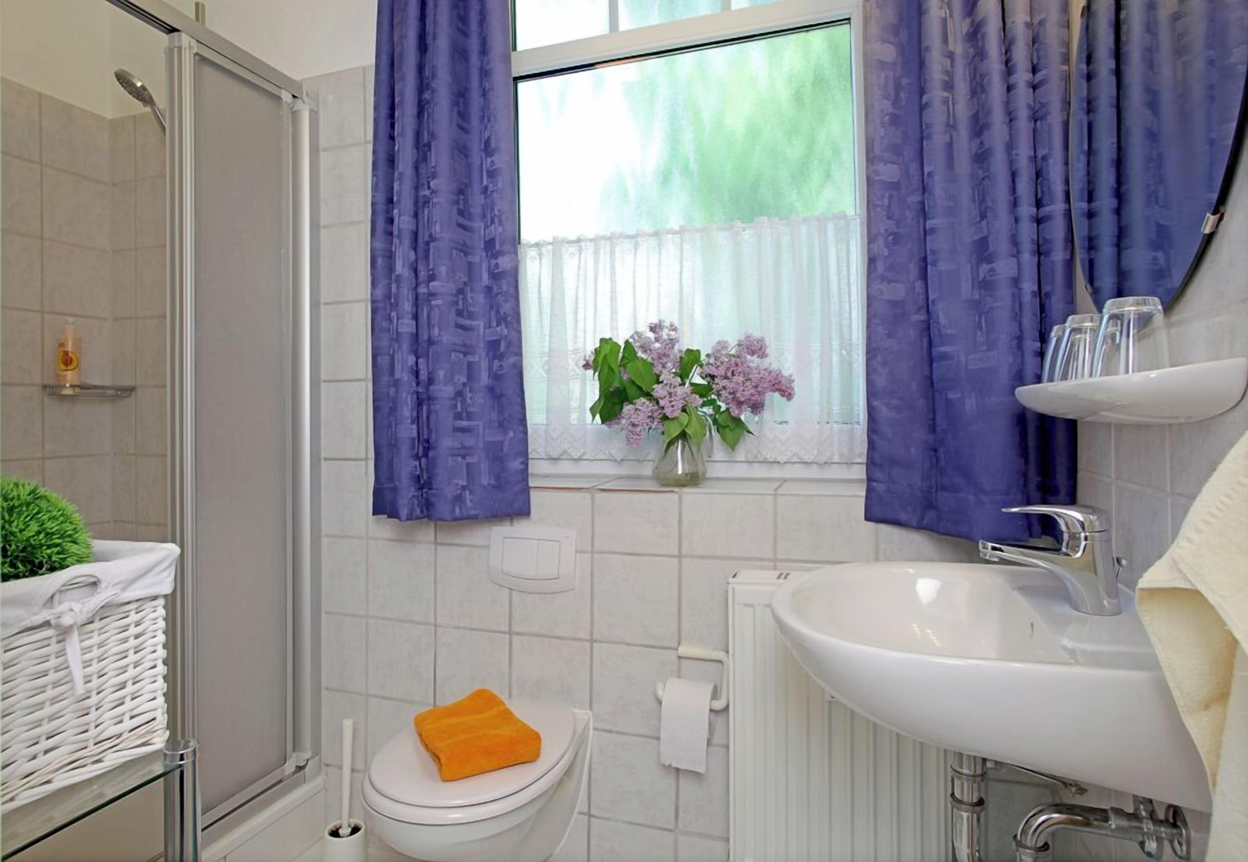 Ein Badezimmer mit Dusche, Toilette, Waschbecken und einem Fenster mit Vorhängen.