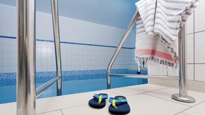 Zona de piscina amb una escala metàl·lica, una tovallola i un parell de xancles al terra.