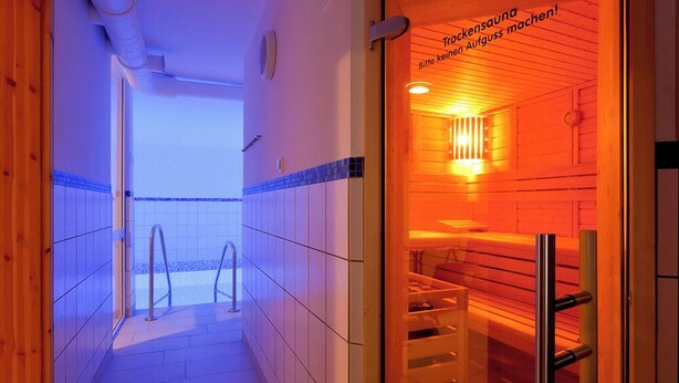 Un espai de sauna amb parets de fusta i un sòl de rajola. Hi ha una porta amb un rètol en alemany.