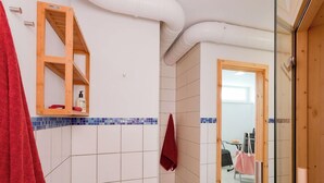 Un bany amb rajoles blanques, una prateleira de fusta amb productes de tocador i una tovallola vermella penjada a la paret.