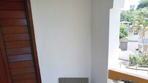 A balcony with wicker furniture, including two chairs and a small table, and a wooden door. - Tropical Paradise (Bridgetown)