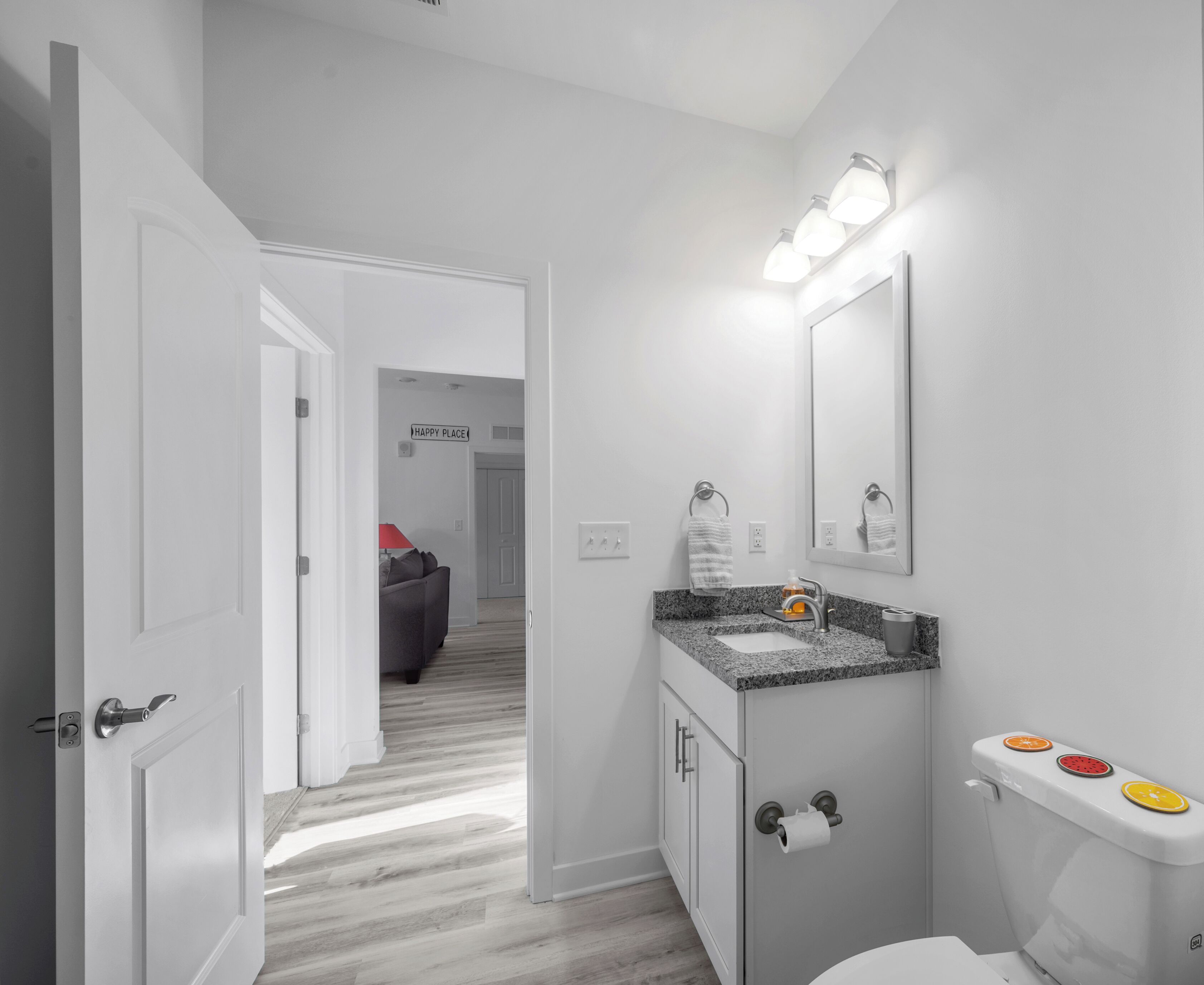 Een moderne badkamer met een wit wastafel, een spiegel en een toilet. Er is een gang die naar een andere kamer leidt.