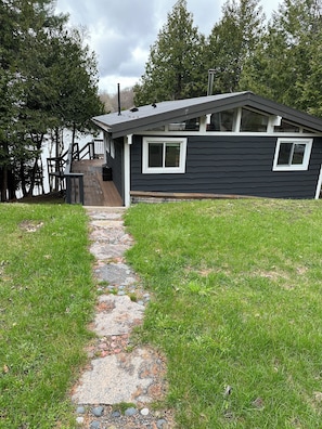 Uma casa moderna com varanda, caminho de pedra e vista para árvores e água.