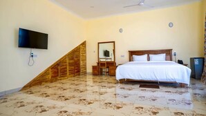 Un dormitorio con cama, televisión montada en la pared, escalera de madera y ventilador de techo.