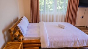 Una habitación con una cama de madera, un taburete pequeño de madera y una ventana con cortinas.