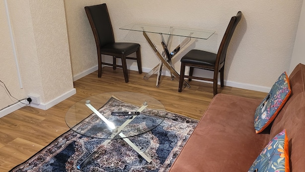 Una sala de estar con una mesa de centro de vidrio, dos sillones, un sofá y un tapete estampado.