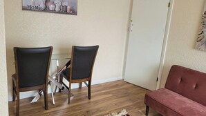 Un comedor con dos sillas y una mesa de vidrio, una puerta cerrada y un sofá rojo.