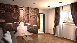 Un salon moderne avec un mur décoré d’une fresque en pierre, un canapé, une table basse et une vue sur une pyramide, visible à travers une fenêtre.