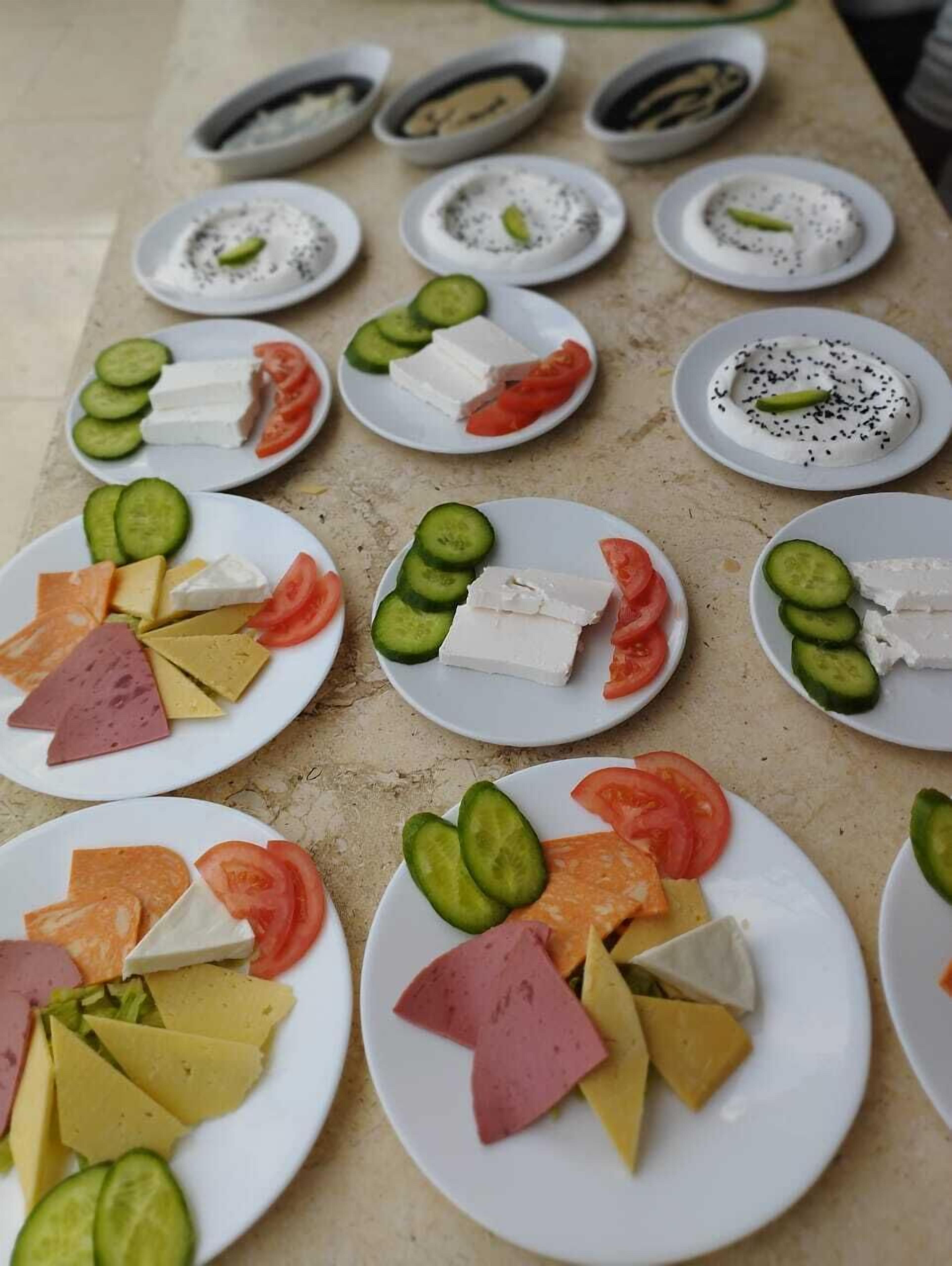 A table with various food items including cheese, tomatoes, cucumbers, and meat arranged on plates.