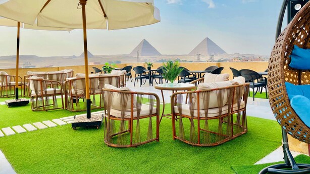 Une terrasse sur le toit, aménagée avec des meubles en osier, un parasol blanc et offrant une vue sur les pyramides.