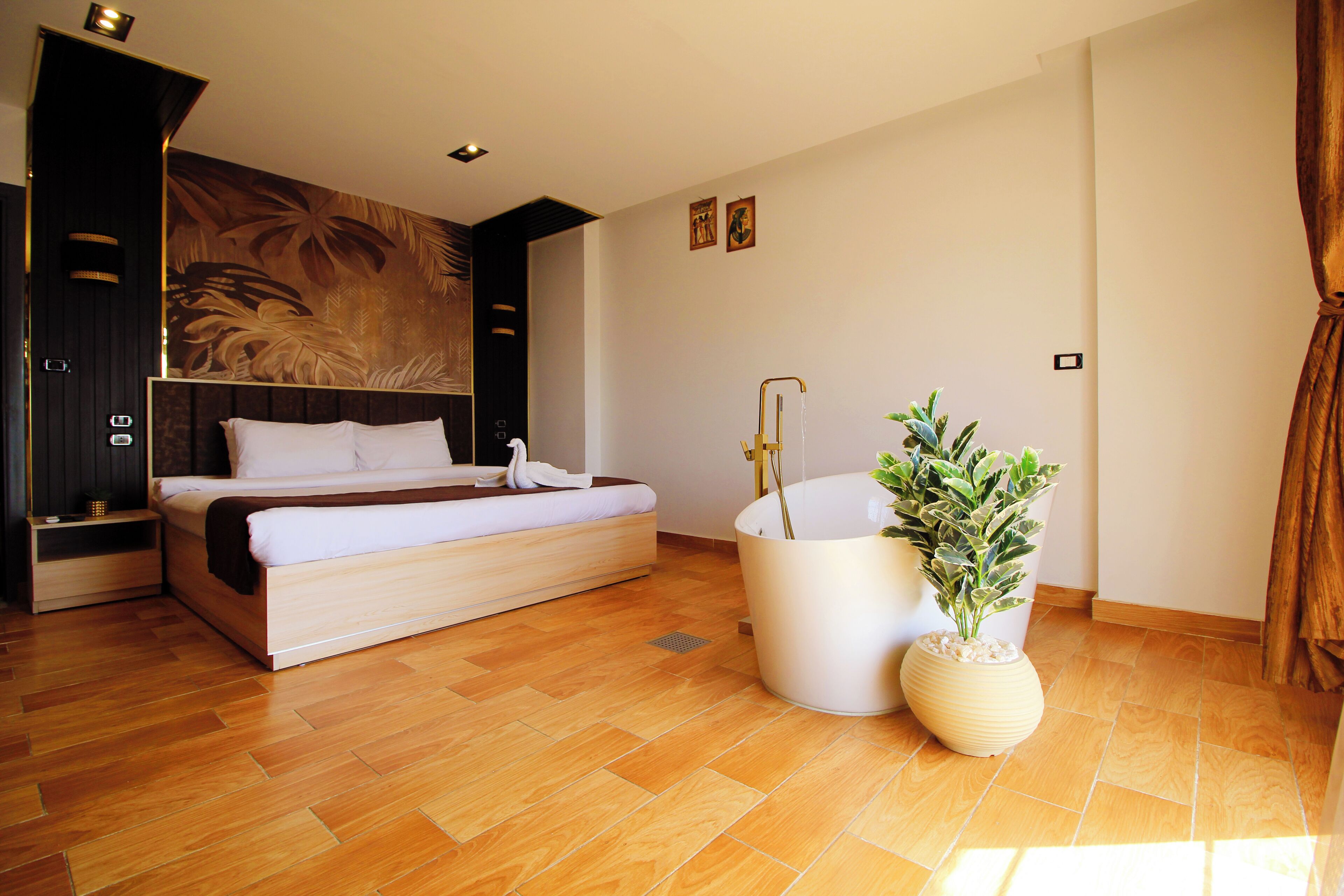 Une chambre à coucher moderne avec un grand lit, une table de chevet, une plante en pot et un luminaire fixé au mur.