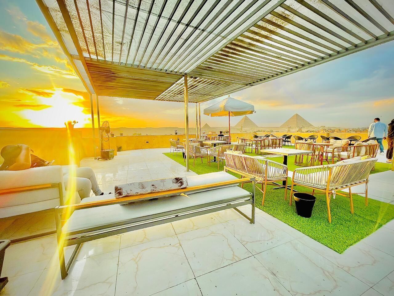 Un lounge en la azotea con vistas a las pirámides, mobiliario exterior y una zona cubierta con mesa y sillas.