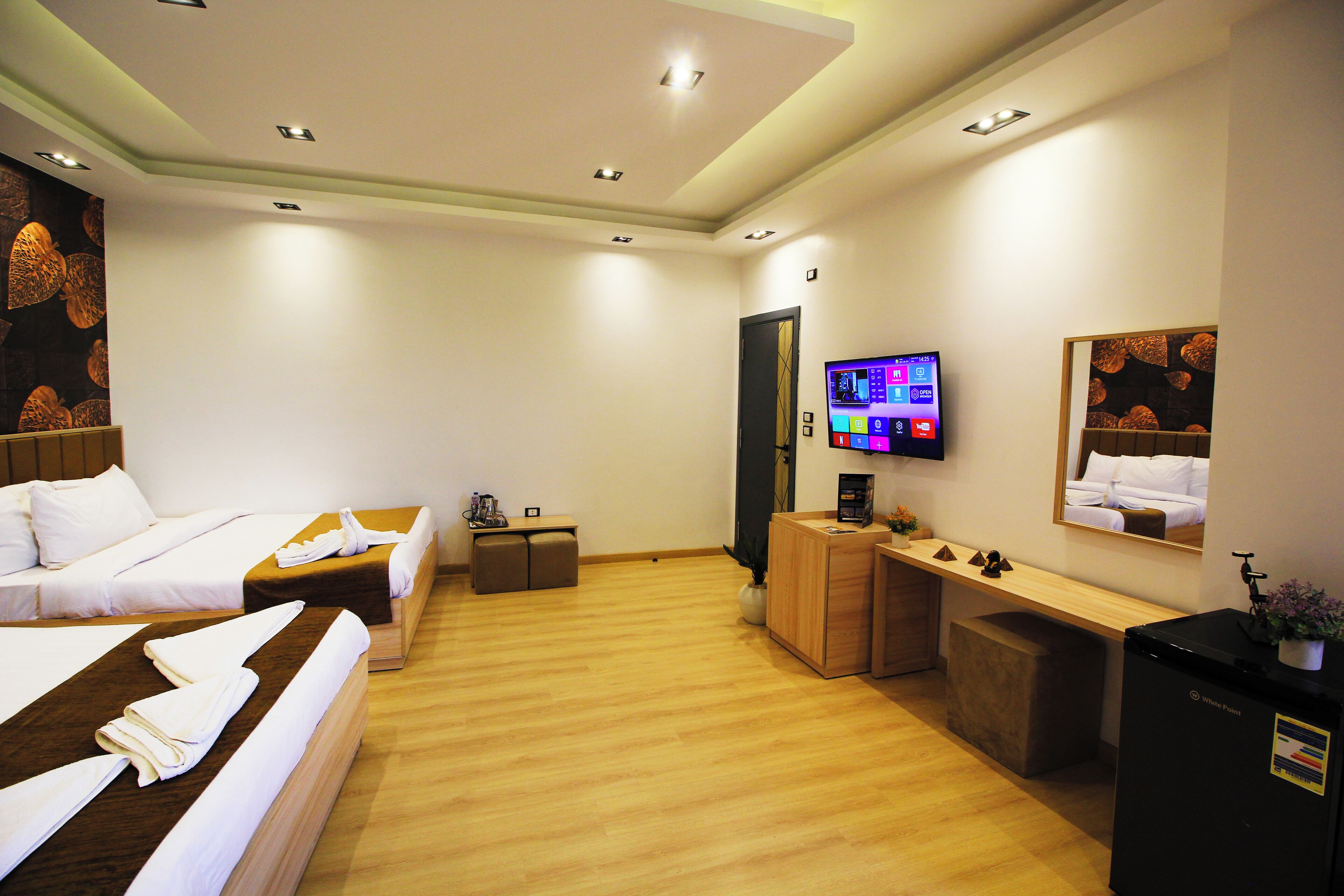 A hotel room with two beds, a desk, a television, and a refrigerator.