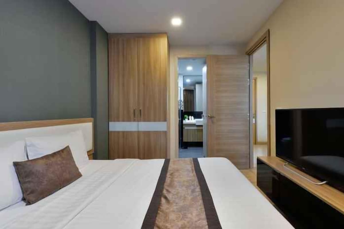 A hotel room with a bed, a television, a wardrobe, and a bathroom in the background.