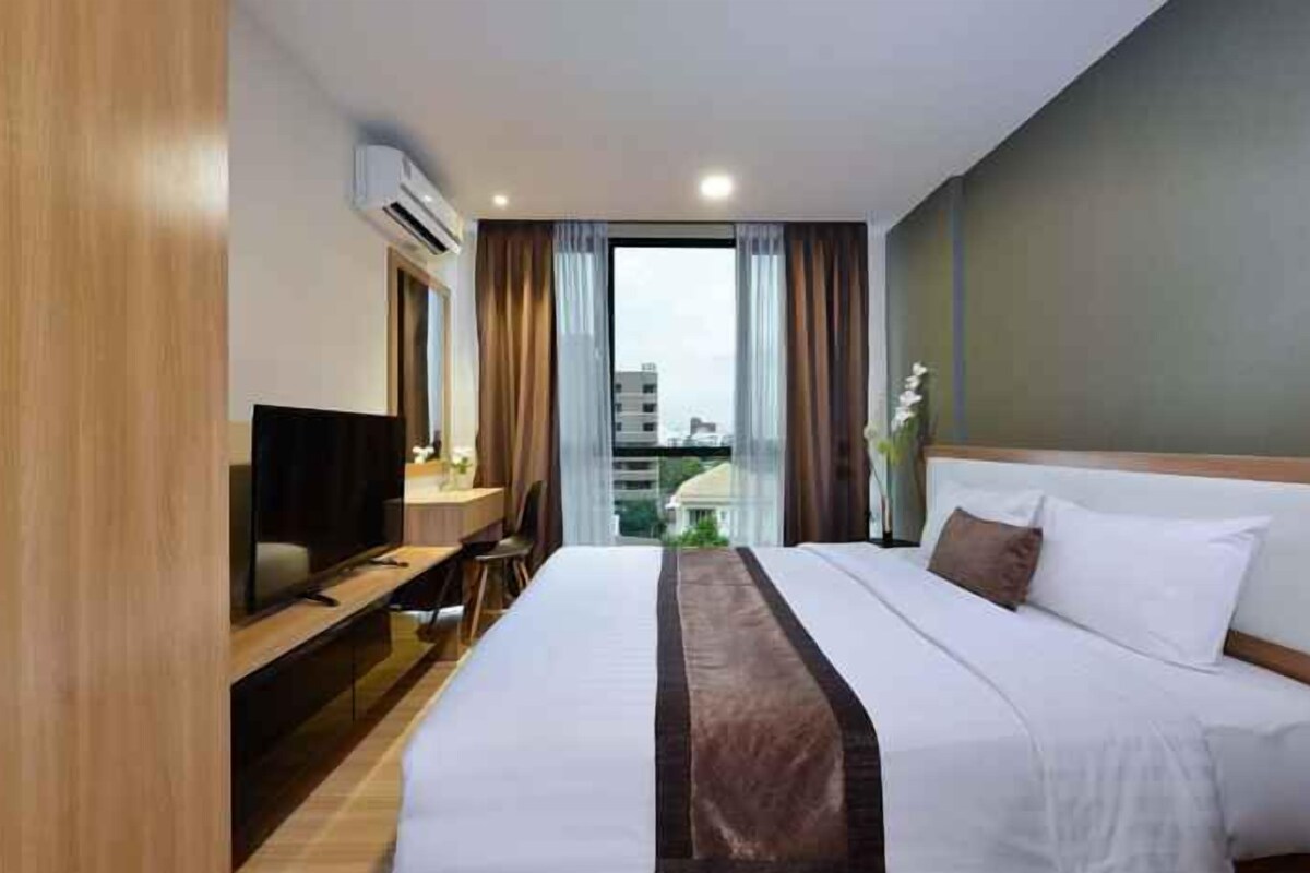 A hotel room with a bed, a desk with a television, and a view of the city.
