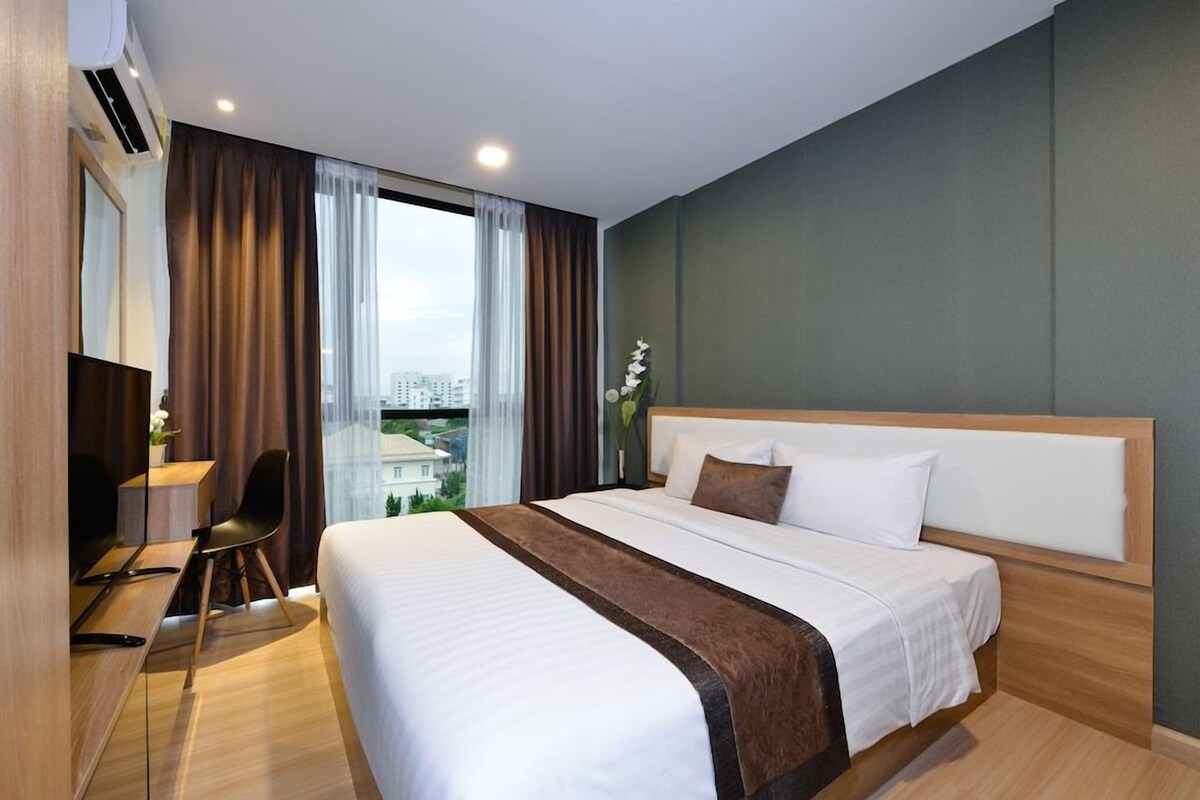 Ein Hotelzimmer mit einem großen Bett, einem Schreibtisch mit Stuhl, Blick auf die Stadt und einem mit Vorhängen versehenen Fenster.