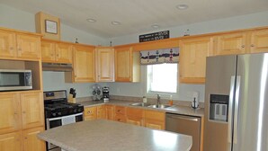 A modern kitchen with wooden cabinets, stainless steel appliances, and a large island with stools. - Cute 3BR/2BA home located in the Village of Clayton with dock rental available (Clayton)