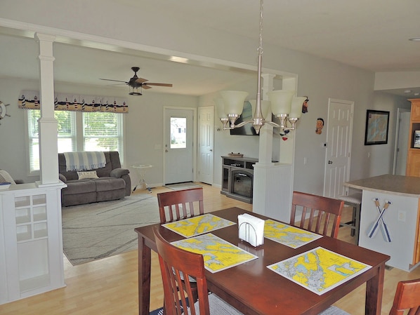 A dining area with a wooden table set for four, a chandelier, and a view into the living room.