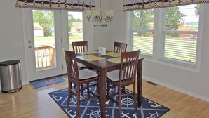 A dining room with a wooden table, four chairs, a chandelier, and a view of a backyard through large windows. - Cute 3BR/2BA home located in the Village of Clayton with dock rental available (Clayton)