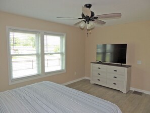 A bedroom with a bed, a dresser, a TV, and a ceiling fan.