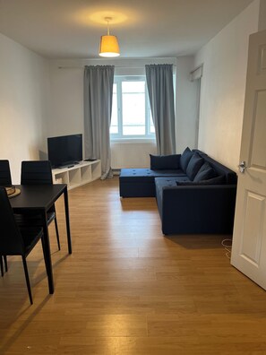 Cozy living space with a sofa, flat-screen TV, dining table, and wooden floor.