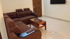 Ein Wohnzimmer mit einem braunen Ecksofa, einem Holztisch und einem an der Wand montierten Fernseher.
