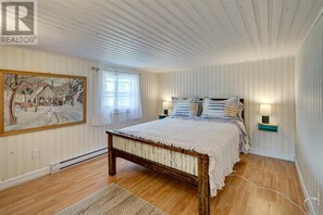 A bedroom with a wooden bed, a painting on the wall, and two bedside lamps. - Renovated 3 Bed Home overlooking Conception Bay in Carbonear, NFLD (Carbonear)
