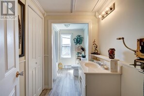 A narrow hallway with a white door, a white sink, and a mirror with a light fixture. - Renovated 3 Bed Home overlooking Conception Bay in Carbonear, NFLD (Carbonear)