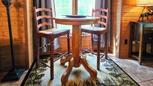 Un intérieur en bois avec une table ronde et deux chaises, une lampe et un tapis orné d’un motif d’arbre.
