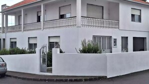 Un edificio de dos pisos con fachada blanca, varias ventanas con contraventanas y un balcón con barandilla.