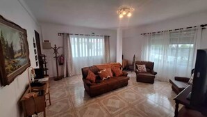 Una sala de estar con un sofá, sillones, una mesa de centro, un cuadro, una chimenea y vistas a la calle desde las ventanas.