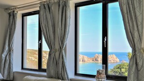 A room with a large window, curtains, a sofa, and a decorative glass vase. - Beachcomber (Penzance)